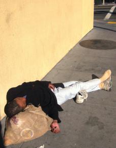 A homeless woman rests on the sidewalk in San Francisco